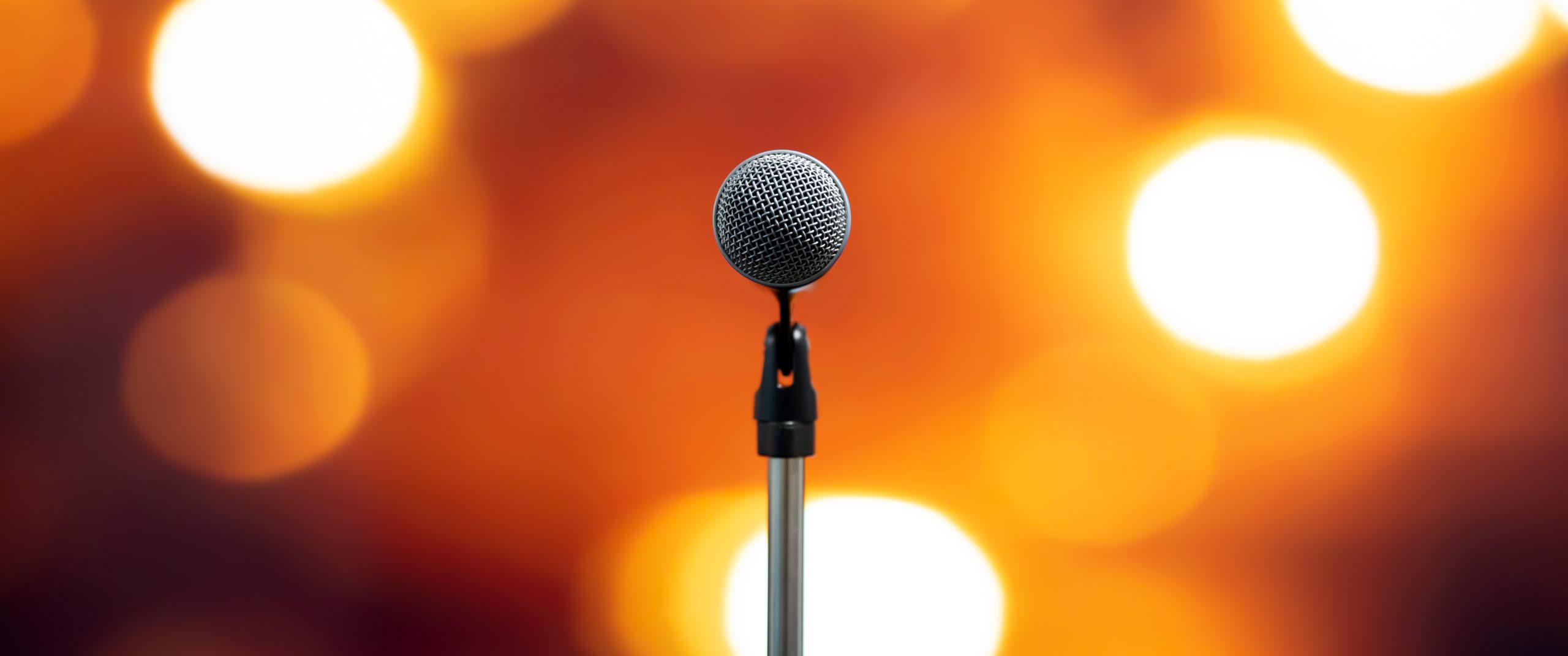 Närbild på en mikrofon framför en suddig bakgrund med lampor riktade mot scenen
