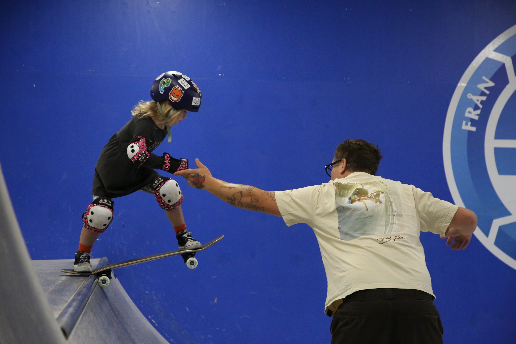 Ung skateboardåkare med skydd åker bräda. Håller hand på instruktör.