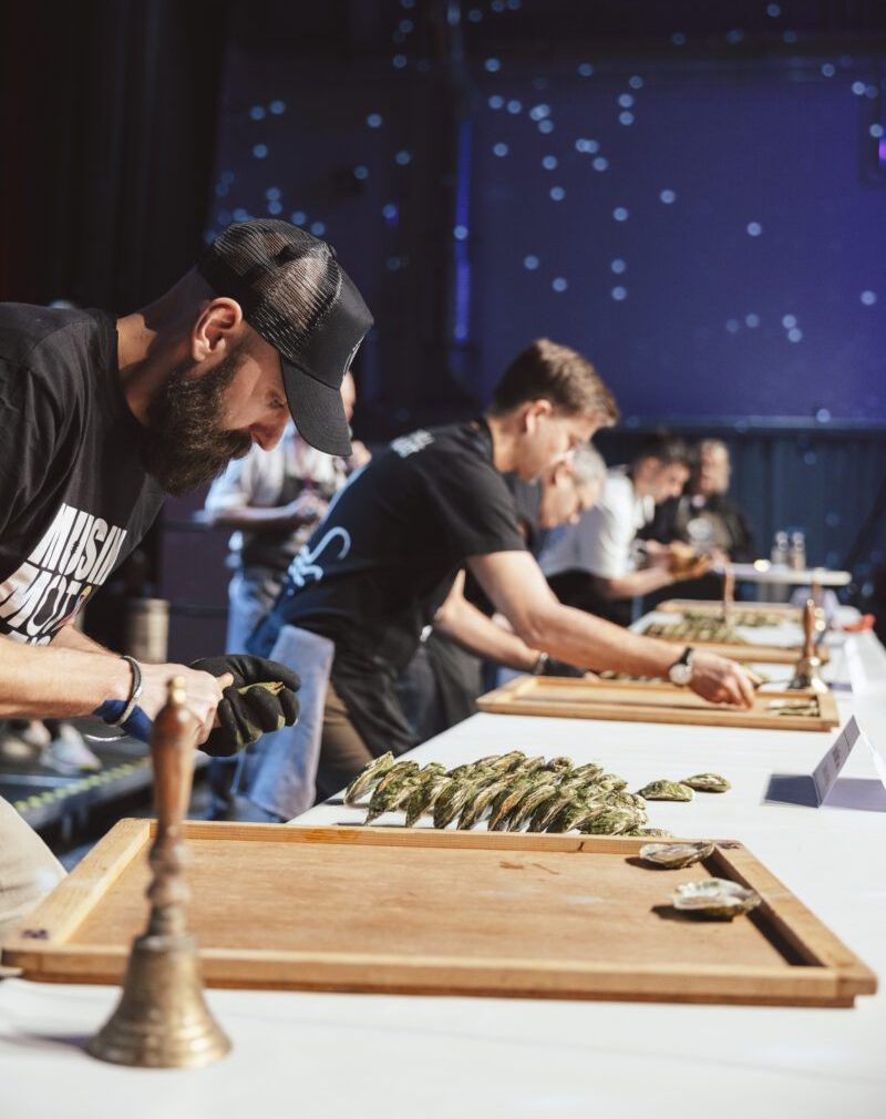 Tävlande lutar sig över ett bord och öppnar ostron